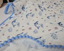 Load image into Gallery viewer, Thin muslin blanket in white with blue dolphins and blue pom pom ribbon