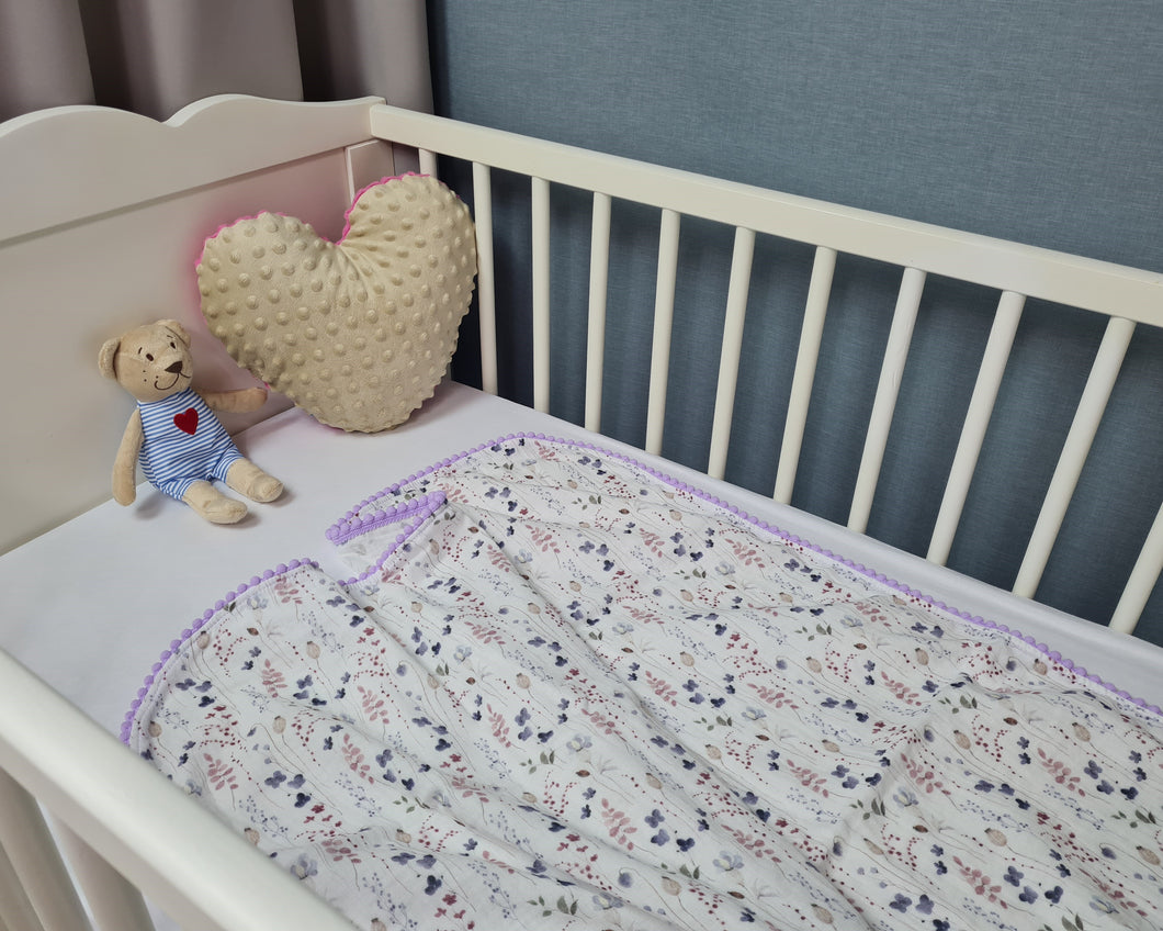 Thin muslin blanket in white with meadow flowers and purple pom pom ball ribbon