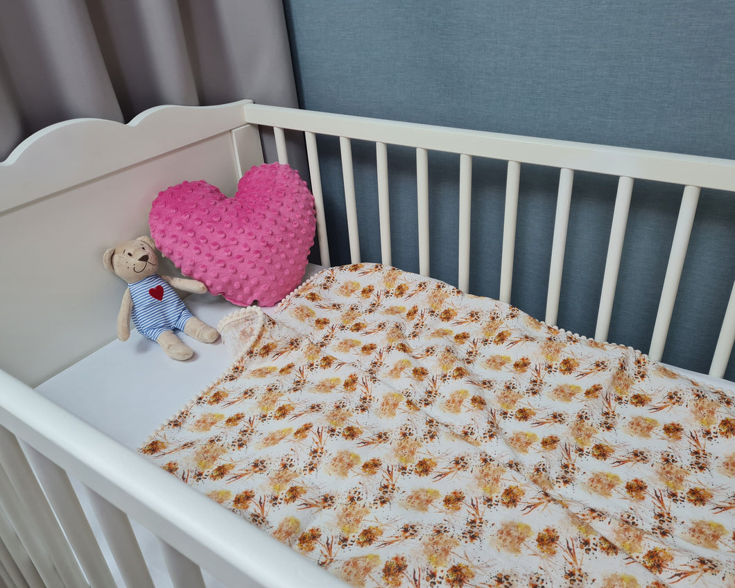 Thin muslin blanket in shades of orange with meadow flowers and beige pom pom ball ribbon