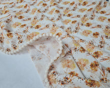 Load image into Gallery viewer, Thin muslin blanket in shades of orange with meadow flowers and beige pom pom ball ribbon
